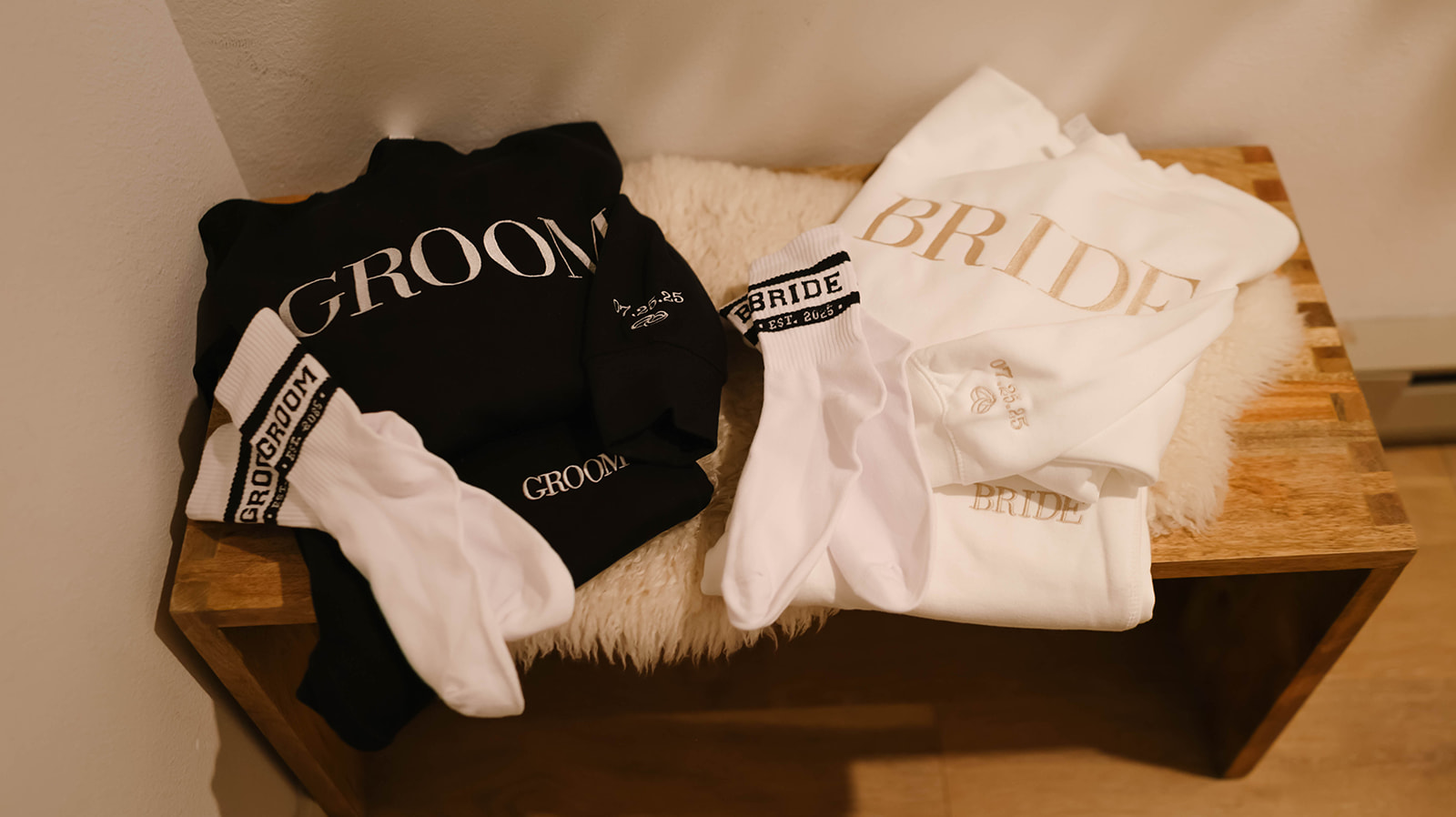 Bride and groom sweatshirts and socks laid out on a wooden bench, cozy details for wedding morning.