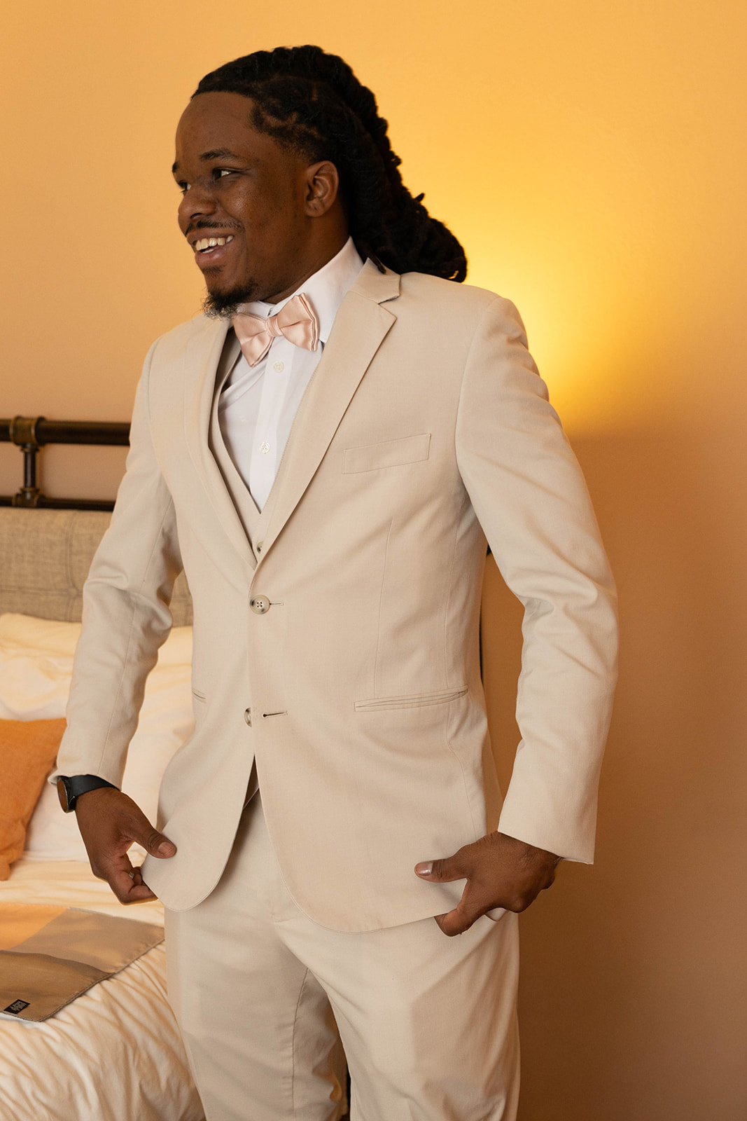 Groom preparing for his wedding day, smiling in his cream suit and blush bow tie, a sweet moment that sparks thoughtful elopement ideas.