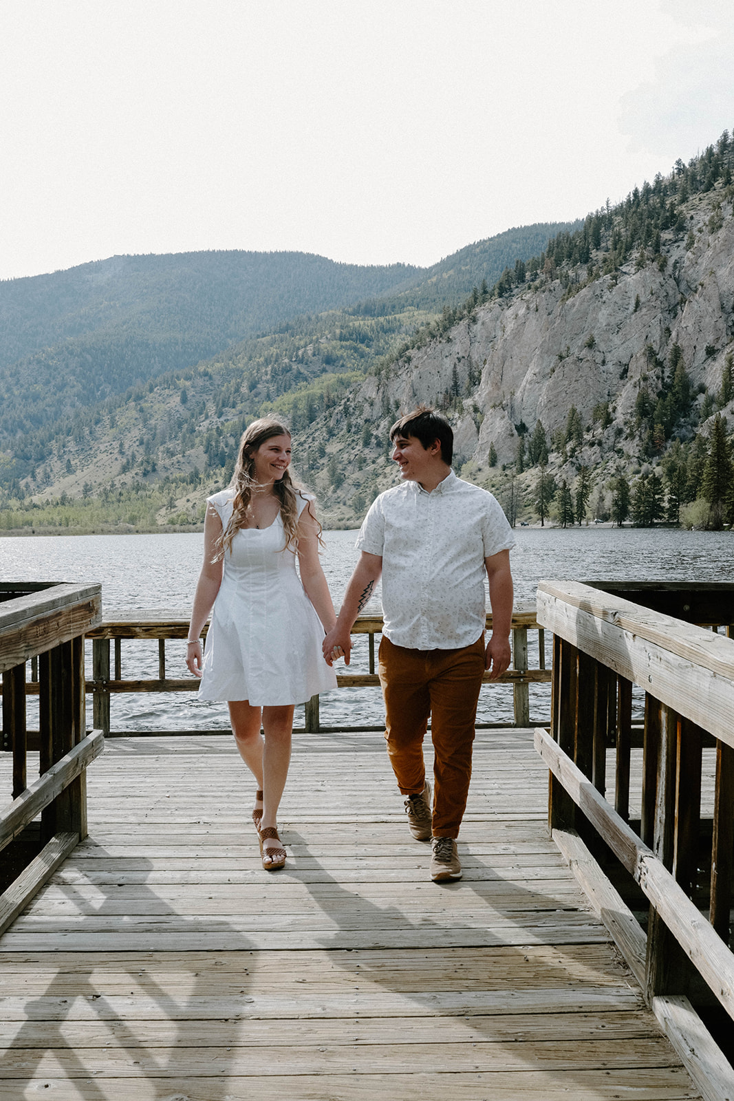 Couple walking side by side on a lakeside dock with mountains and water in the background in Buena Vista, Colorado.