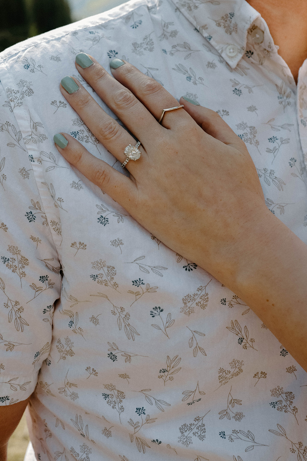 Close-up of an engagement ring on a hand resting against a patterned shirt.