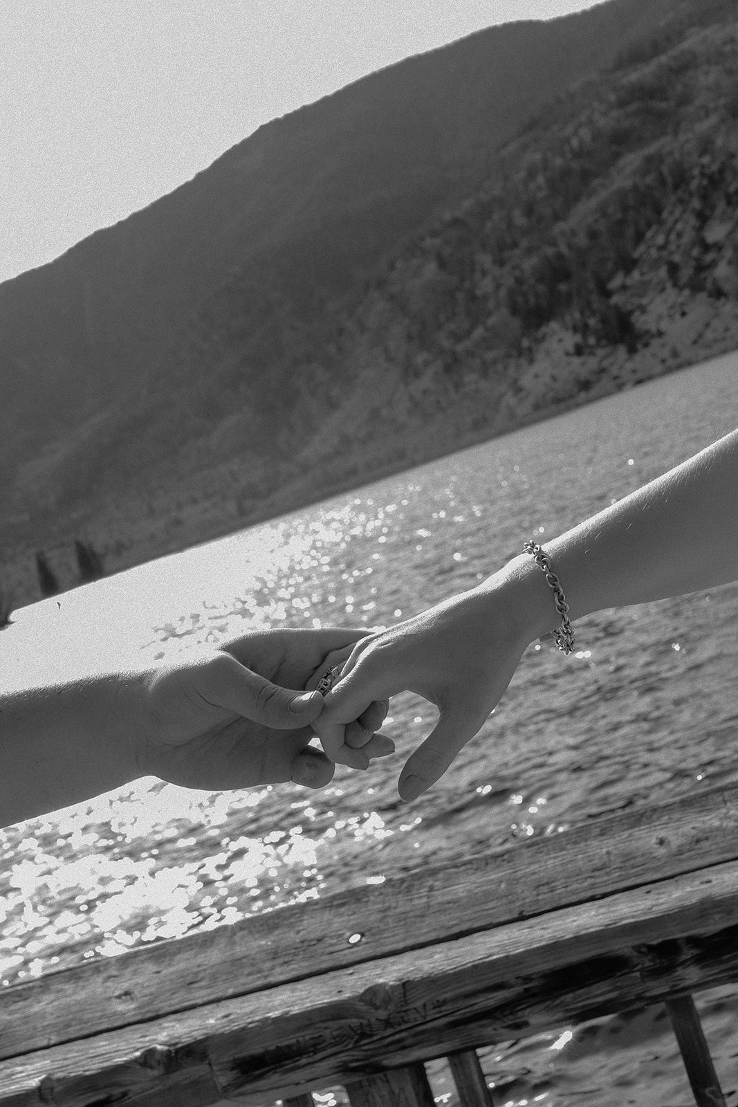 Black and white close-up of two hands gently linking pinkies above the water.