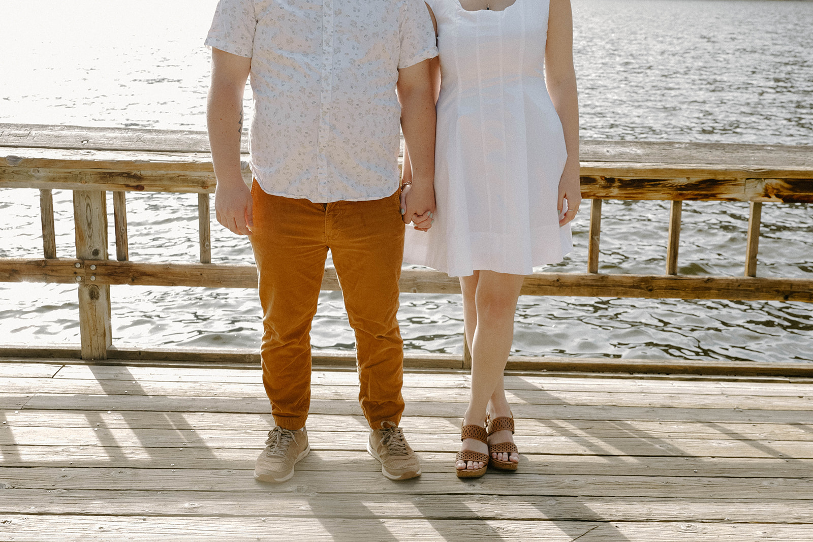 Close-up of a couple holding hands on a wooden dock with the lake glistening in the background in Buena Vista, Colorado.