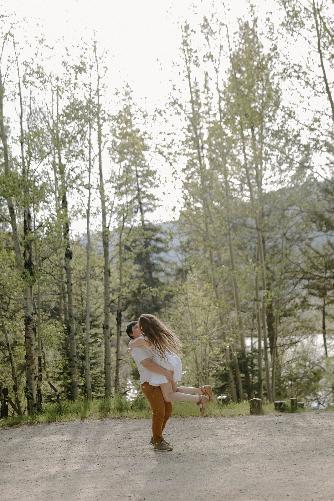Groom lifting his fiancée into the air for a playful kiss among the tall trees in Buena Vista, Colorado.