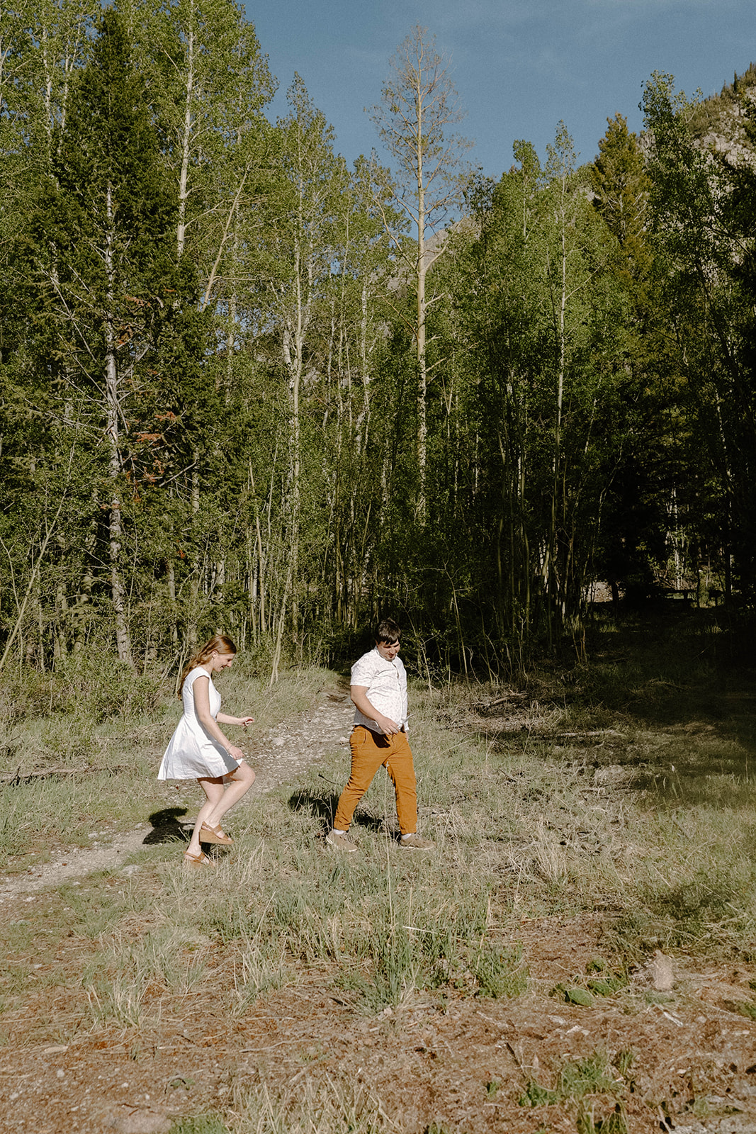 Bride-to-be in a white dress walking through the forest hand in hand with her fiancé.