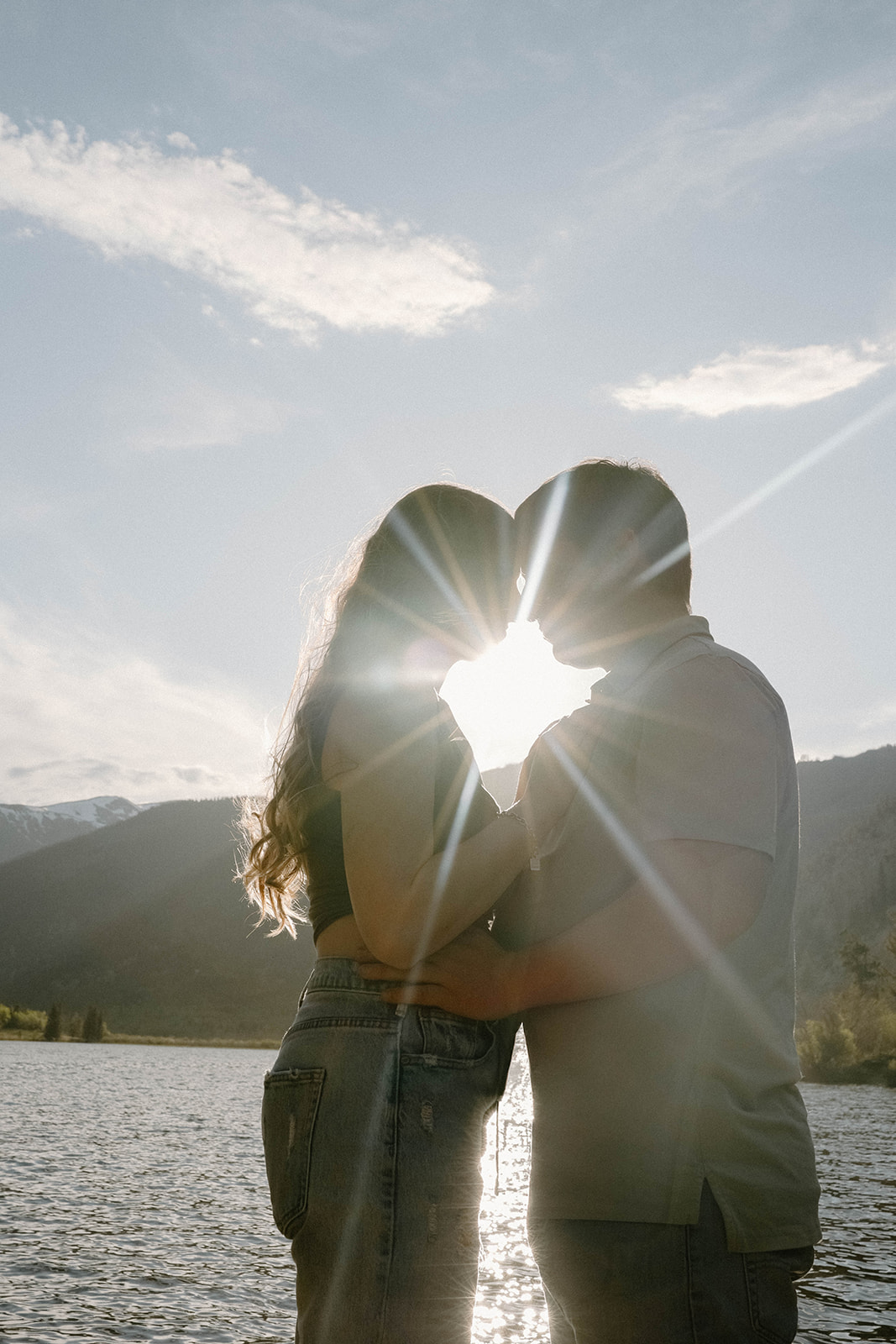 Silhouette of a couple kissing at sunset with sun rays beaming over the lake and mountain peaks in Buena Vista, Colorado.