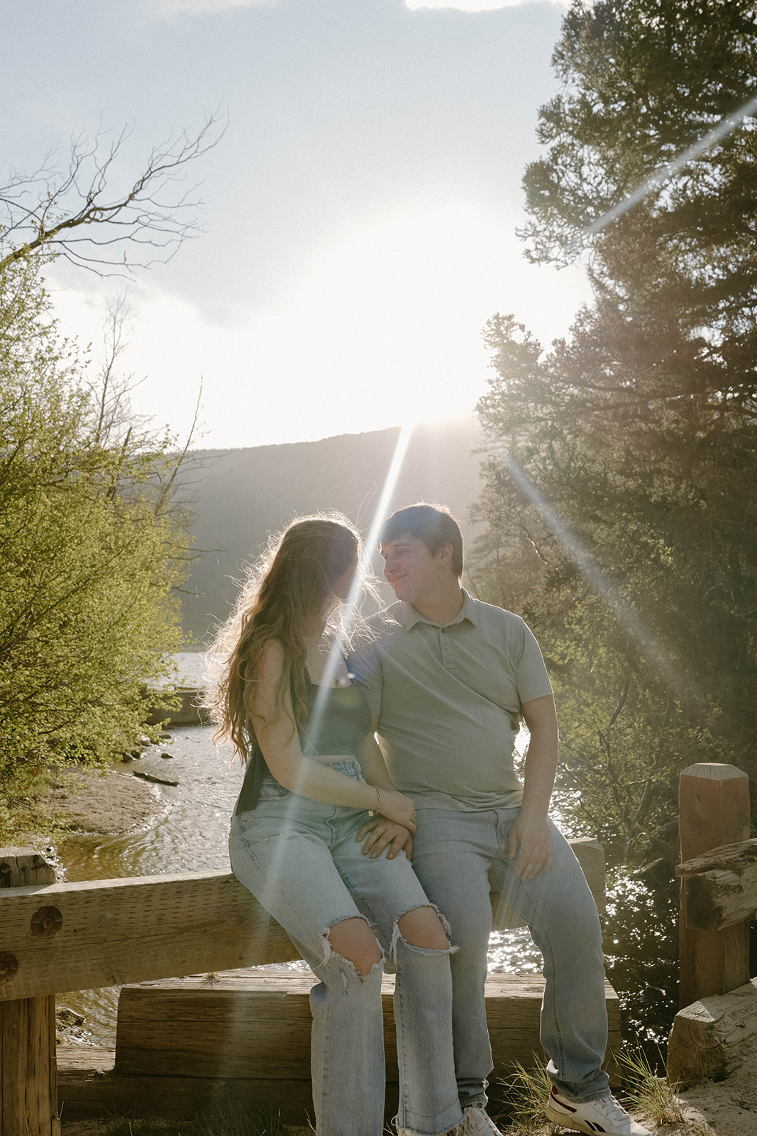 Couple sitting together on a wooden fence by the water, smiling at each other as the sun sets over Buena Vista, Colorado.