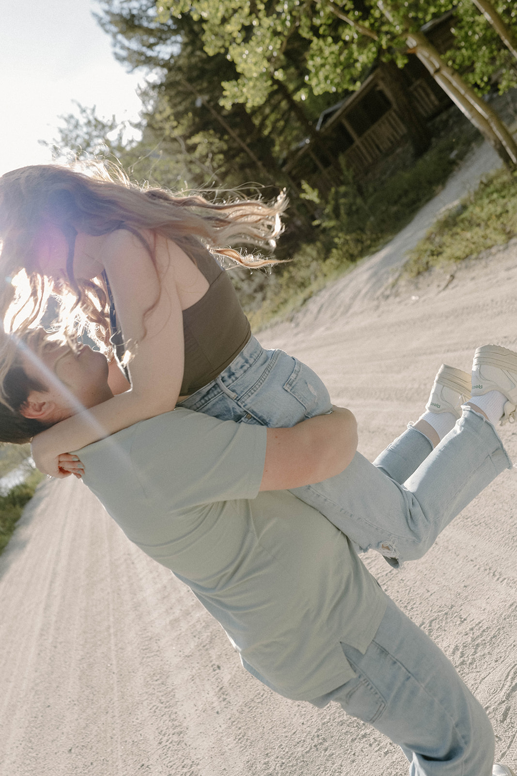 A playful moment of a man lifting his partner into the air on a dirt road, sunlight catching her hair.