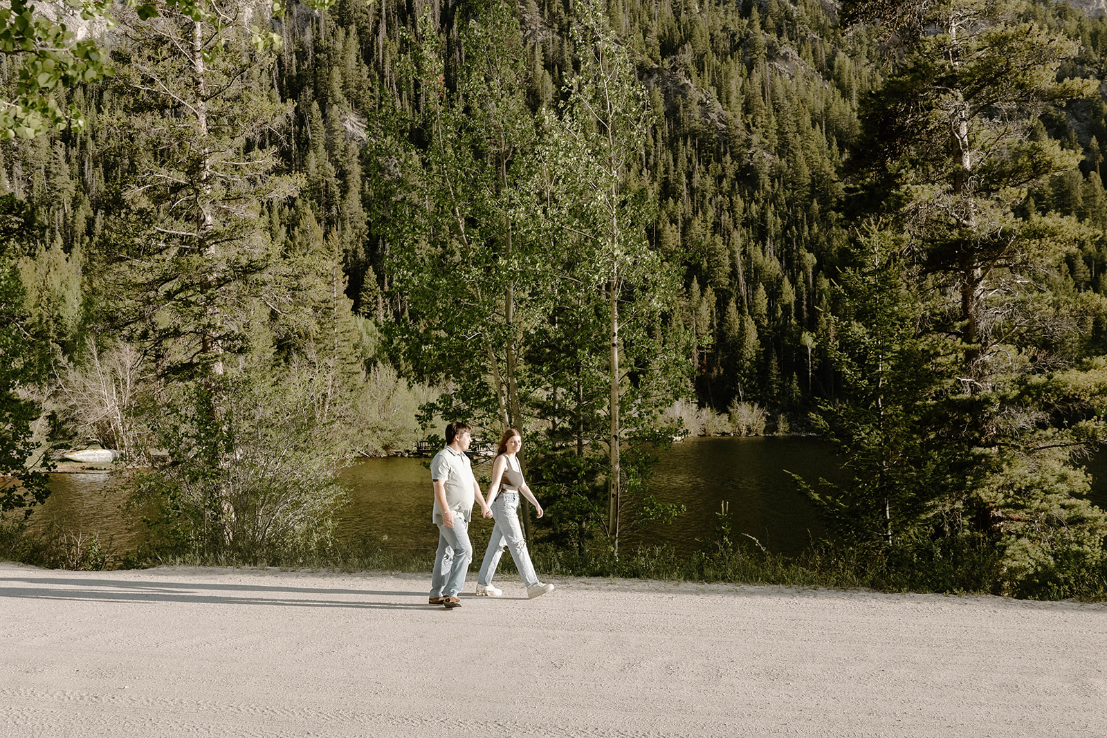 Couple walking hand-in-hand on a quiet lakeside road surrounded by pine trees in Buena Vista, Colorado.