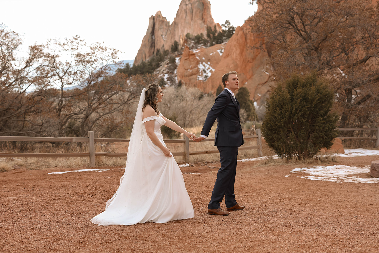A bride and groom holding hands at Garden of the Gods, framed by the park’s iconic red rock formations.