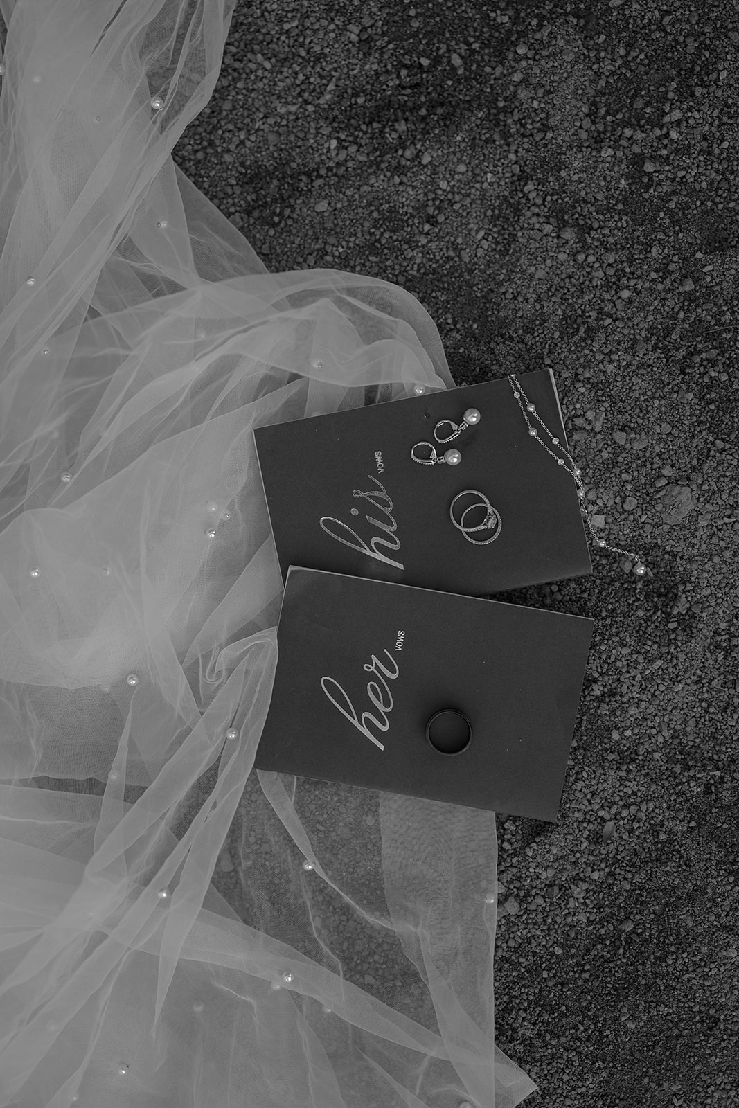 Flat lay of vow books, rings, and jewelry on the ground, with a soft bridal veil adding texture. Details styled by a Colorado wedding photographer.
