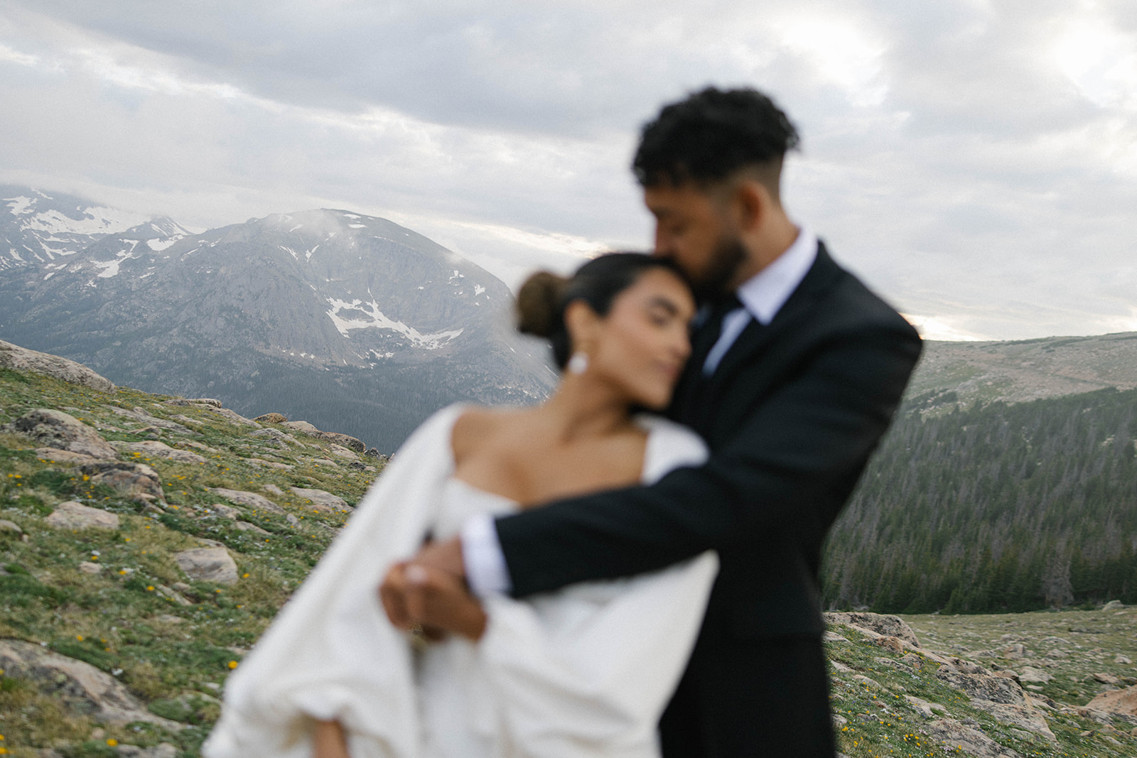 Romantic blurred image of a bride and groom embracing in the mountains, with sweeping alpine views behind them. Documented by a Colorado wedding photographer.