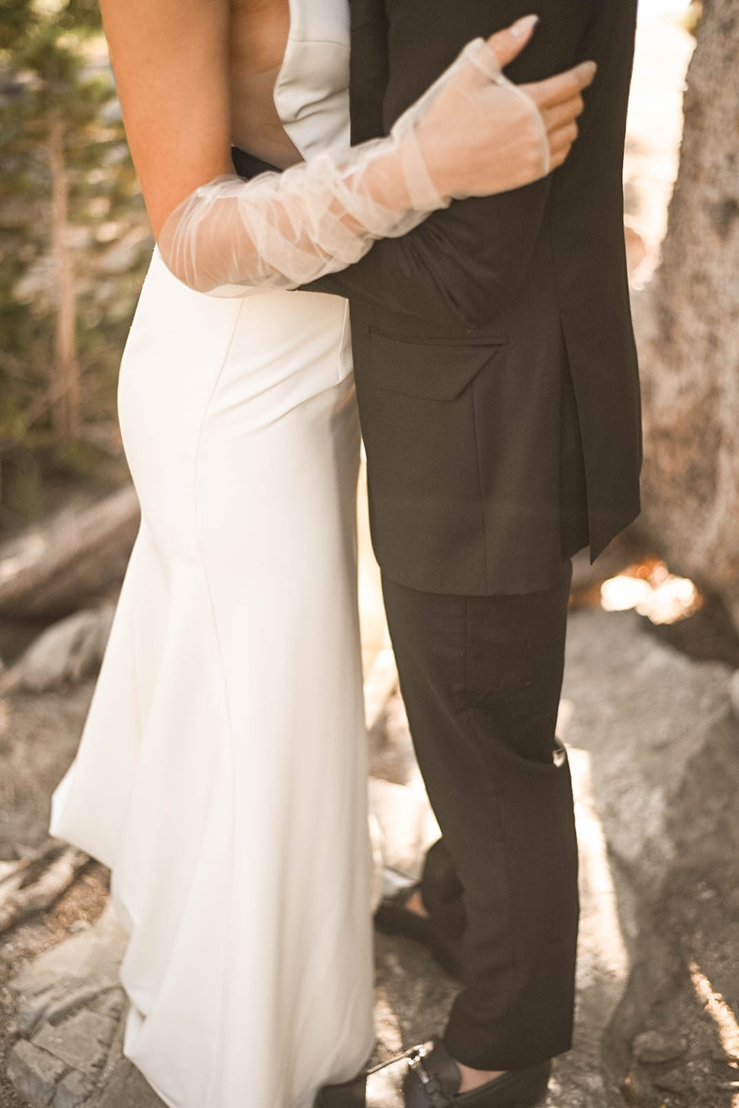Close-up of a bride in a satin gown and sheer gloves embracing her groom in a black suit, captured by a Colorado wedding photographer.