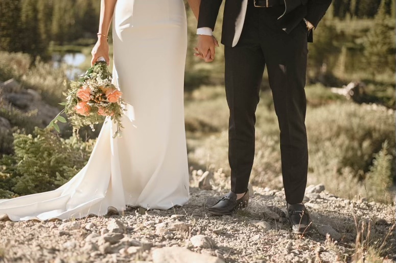 Close-up of a couple holding hands, the bride’s bouquet of peach roses hanging down with her flowing gown. Captured by a Colorado wedding photographer.
