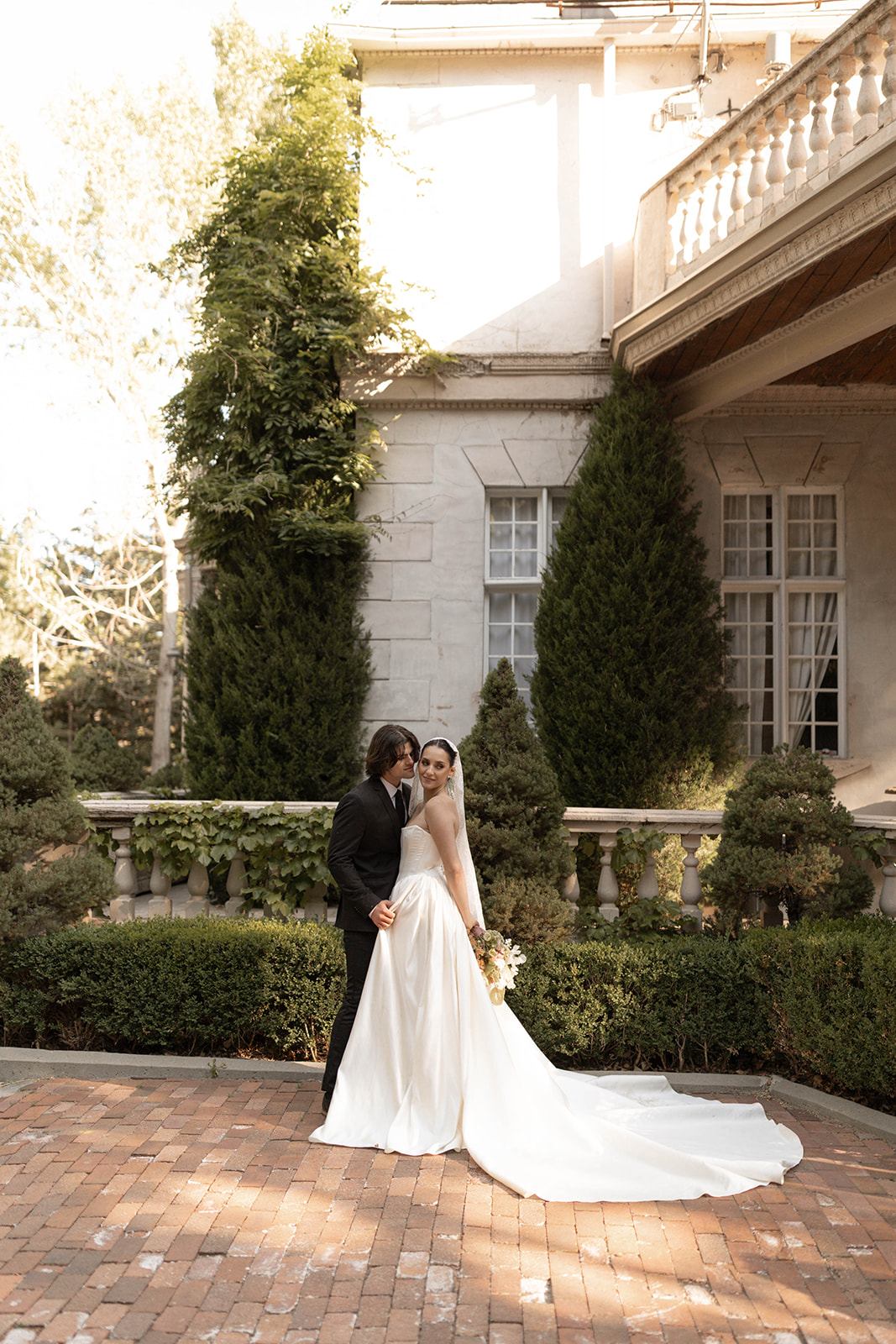 The groom kisses the bride’s temple while sunlight filters through the garden courtyard at La Caille, Utah.
