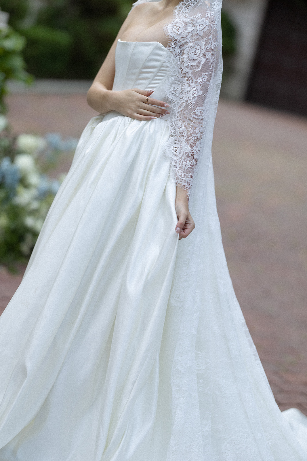 Close-up of a bride in an elegant satin gown with a lace veil draped over her shoulder, softly holding her waist.