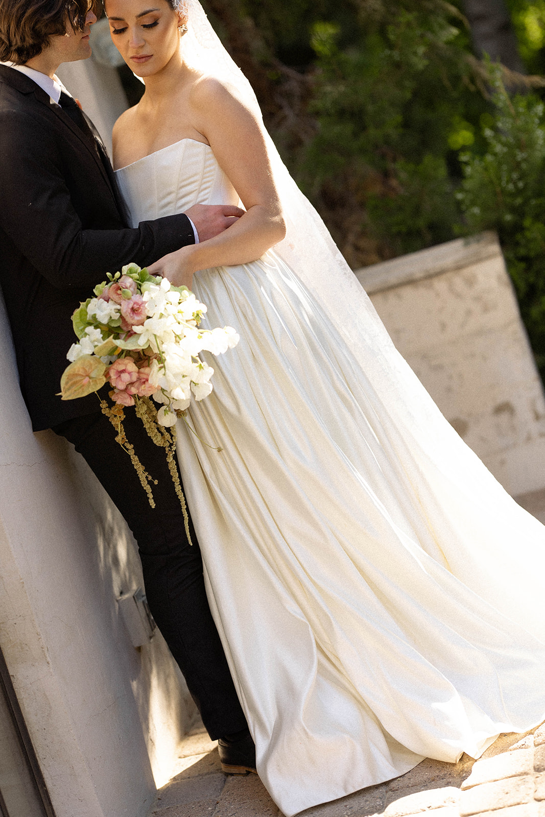 The bride and groom share an intimate moment in soft afternoon light, her full satin skirt catching the glow.