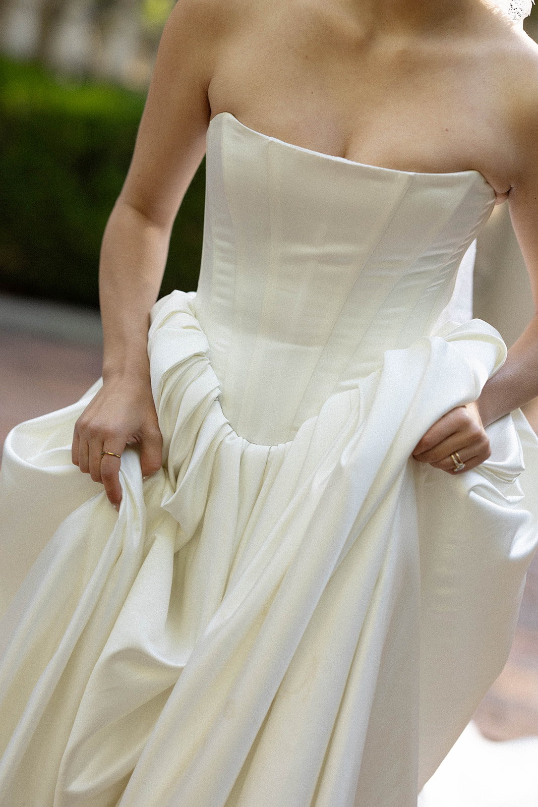 The bride gently lifts her dress as sunlight filters through the trees at La Caille, Utah, showcasing timeless romance.