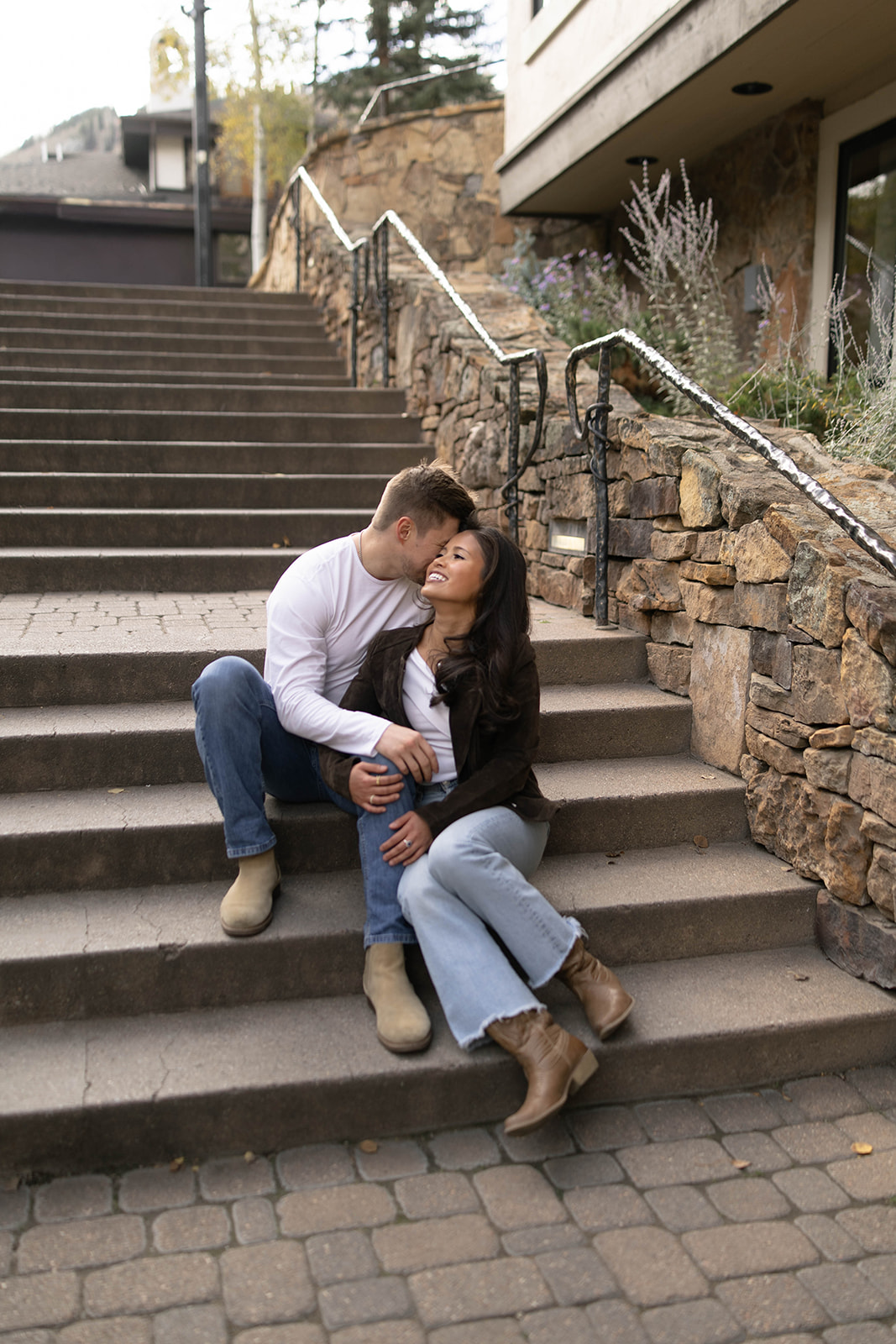 Couple sitting on stone steps as he kisses her forehead during their fall engagement session.