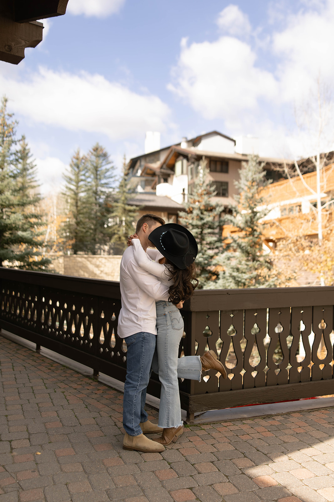 Romantic moment as a couple kisses on a wooden bridge surrounded by evergreens in Vail Village in Colorado.