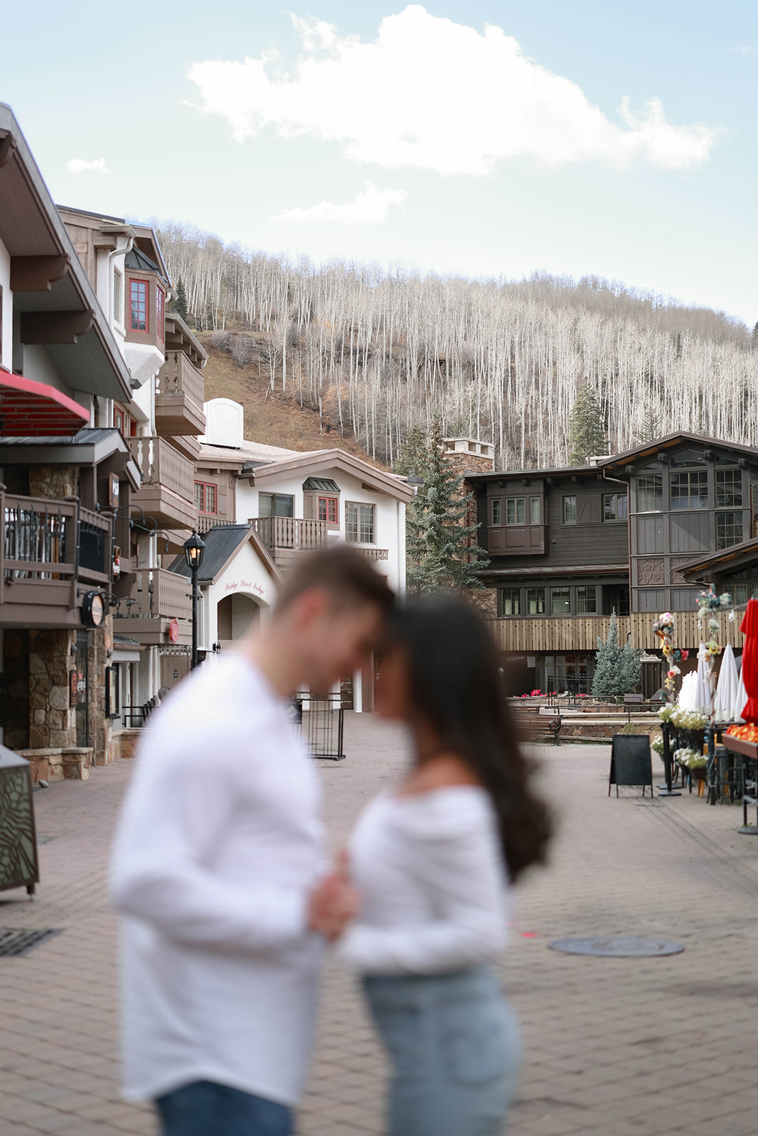 A blurred couple shares a quiet moment while standing in the middle of Vail Village in Colorado with the mountain backdrop.