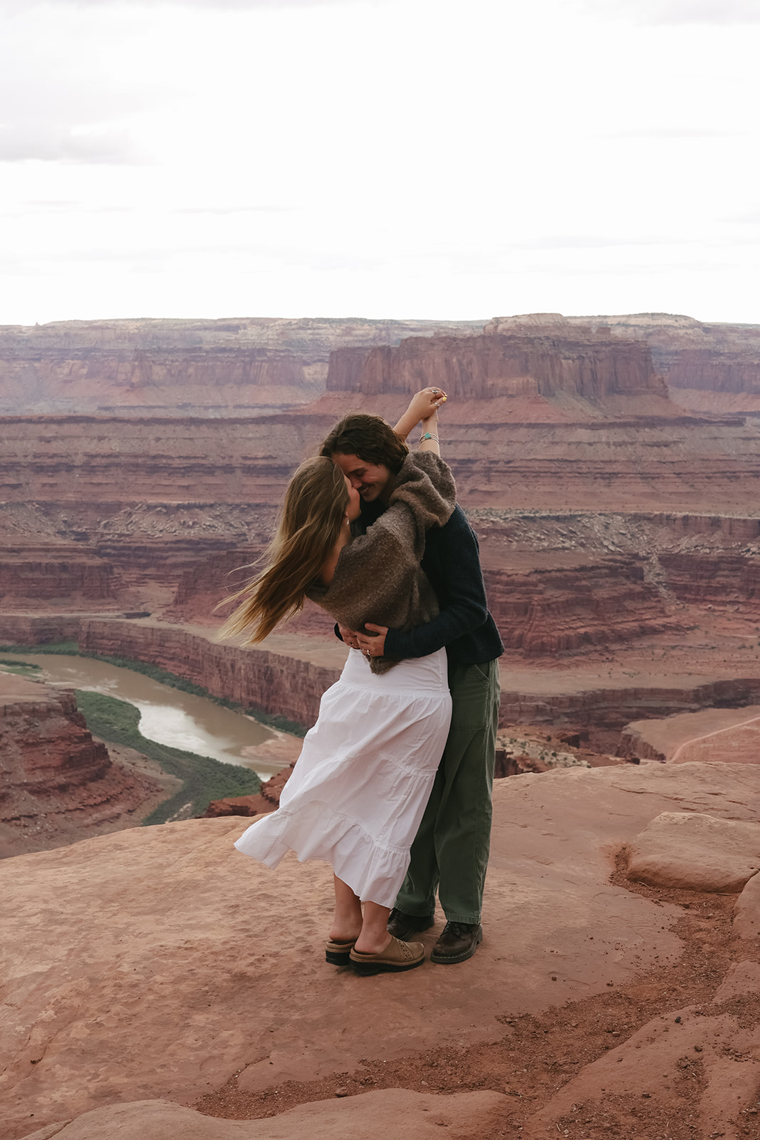 On a desert cliff, the couple embraces in the wind, a dreamy couples photoshoot filled with raw, romantic energy.