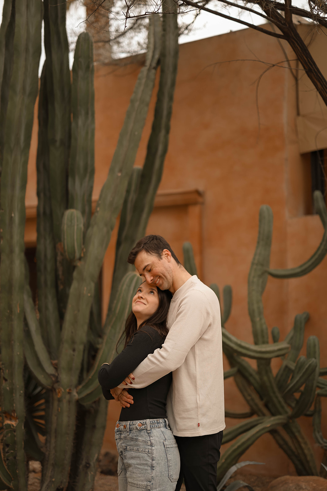 A romantic couples photoshoot under the cacti, where the pair shares a soft embrace in front of terracotta walls.
