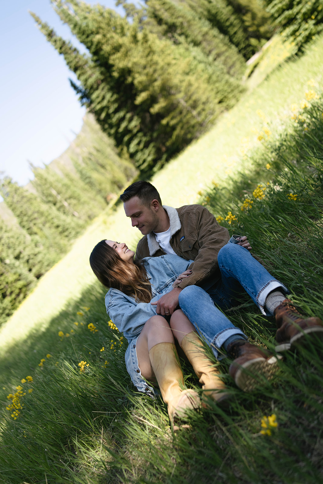 The couple sits together in a field of yellow wildflowers, boots and denim perfectly matching the laid-back summer mountain vibe.
