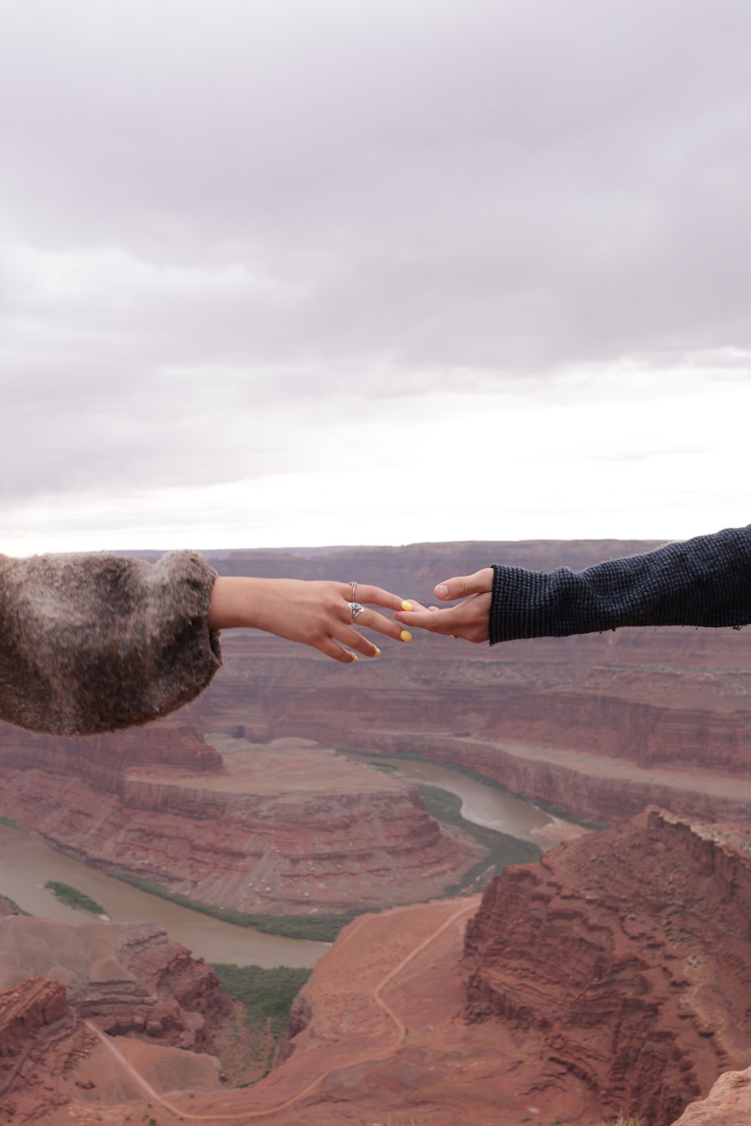 Two hands reach across the canyon view, fingertips just touching against the muted desert backdrop.