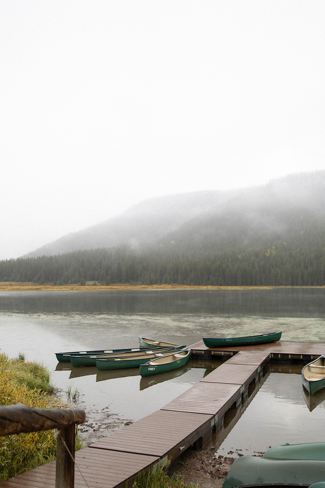 Canoes rest on a fog-covered lake, reflecting the still beauty of the mountains at Piney River Ranch.