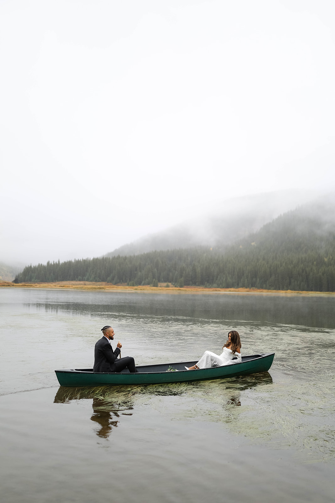 A misty lake view as the couple floats in a canoe, mountains disappearing into the clouds at Piney River Ranch.