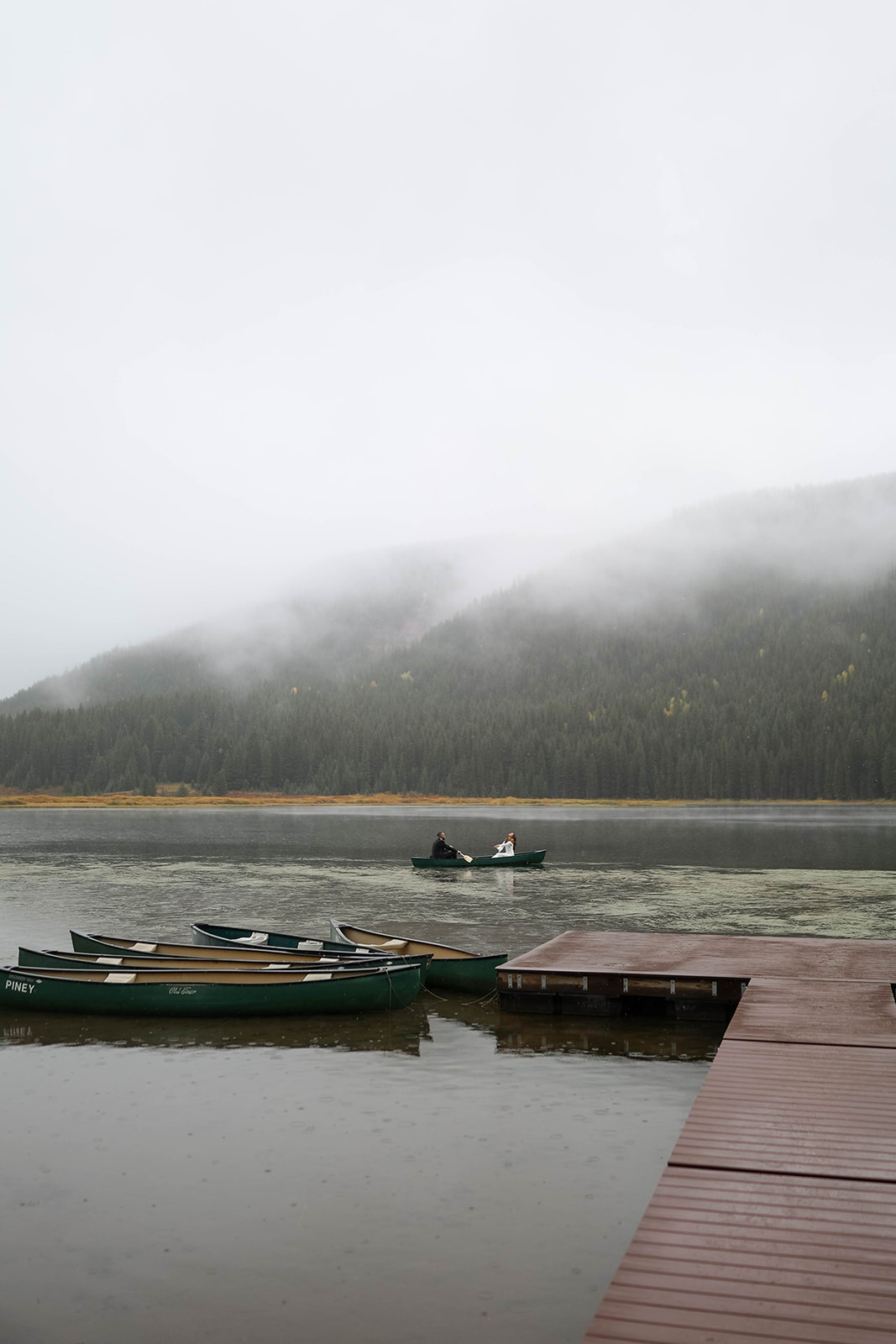 Canoes lined along a quiet dock as a couple glides through the foggy lake, surrounded by the stillness of the Colorado wilderness.