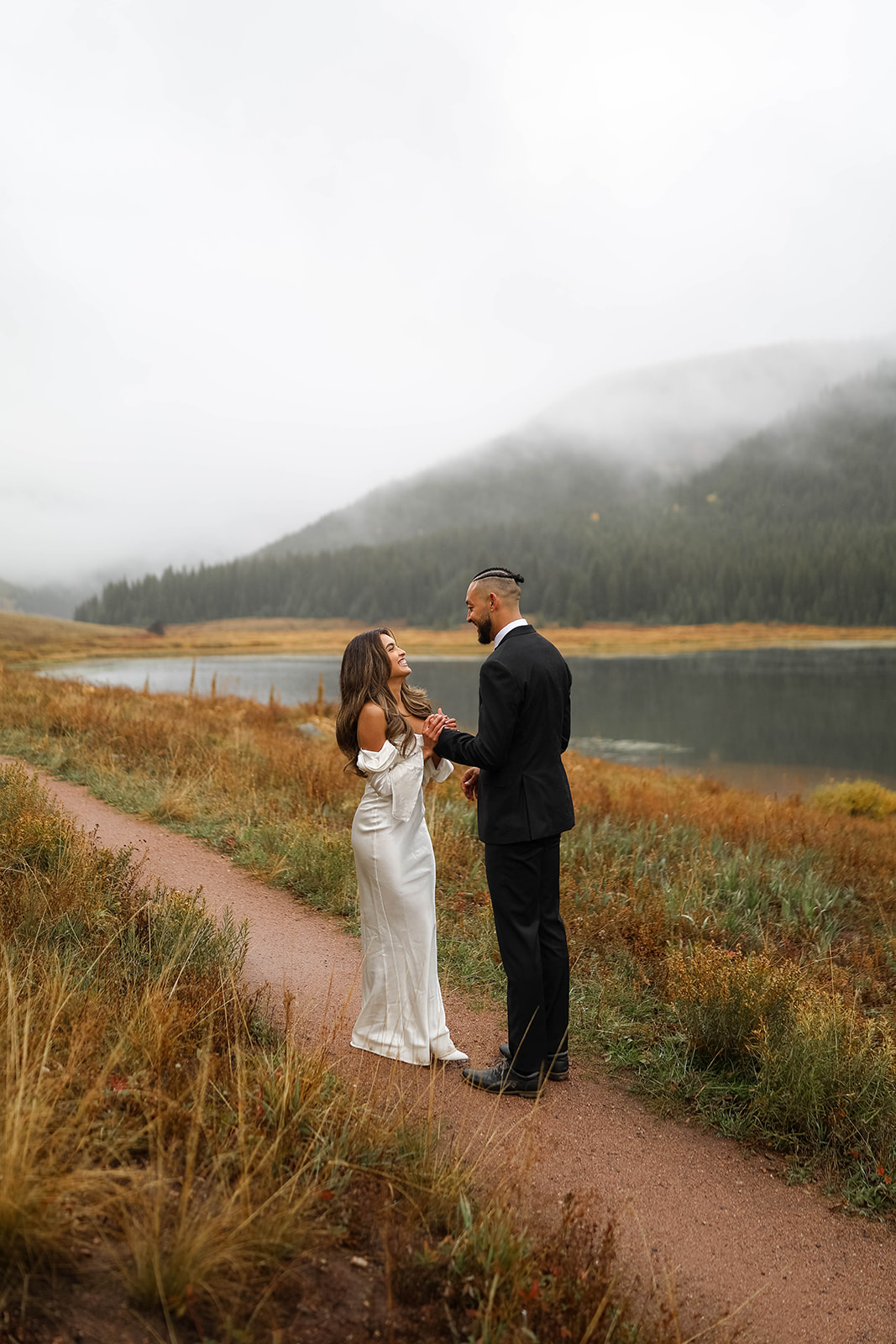 The couple laughs together on a foggy path overlooking the water at Piney River Ranch during their intimate elopement.