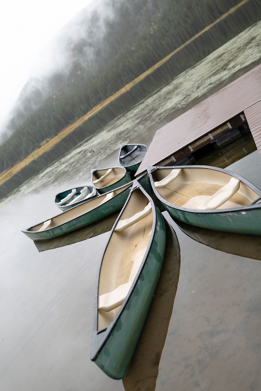 Green canoes float near the dock at Piney River Ranch as fog rolls across the lake and forested hills.