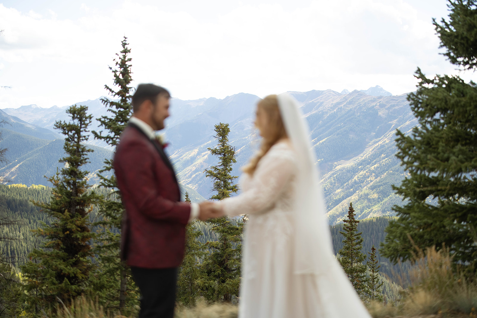 Intentional motion-blur image of the couple holding hands against a backdrop of alpine mountains and evergreen trees.