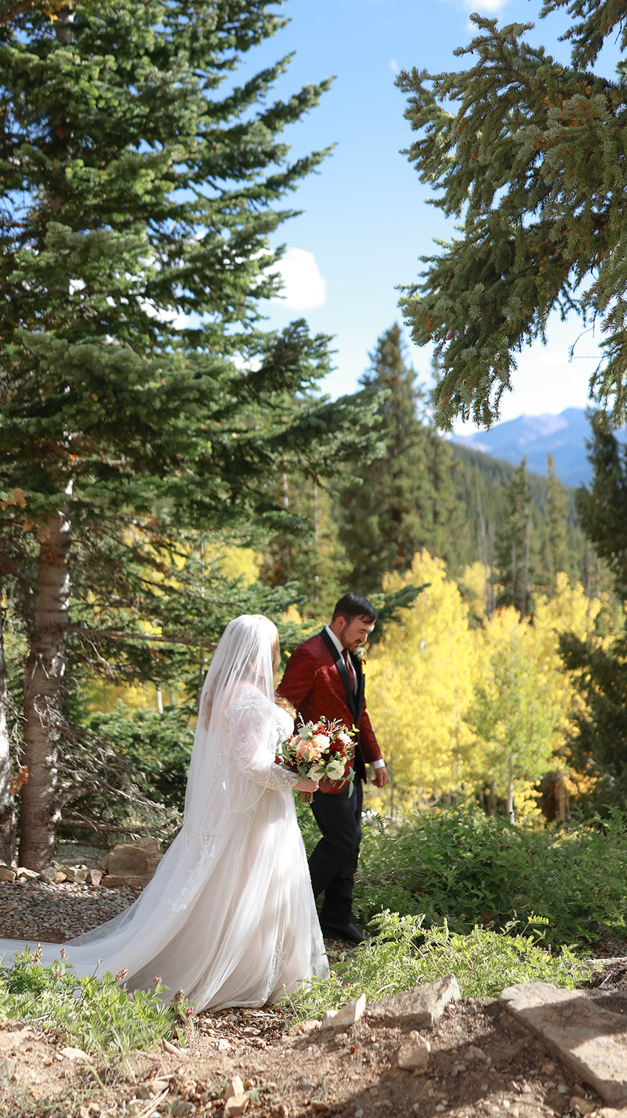 Bride and groom walking together through a pine forest during an intimate aspen elopement, surrounded by golden fall foliage and mountain views.