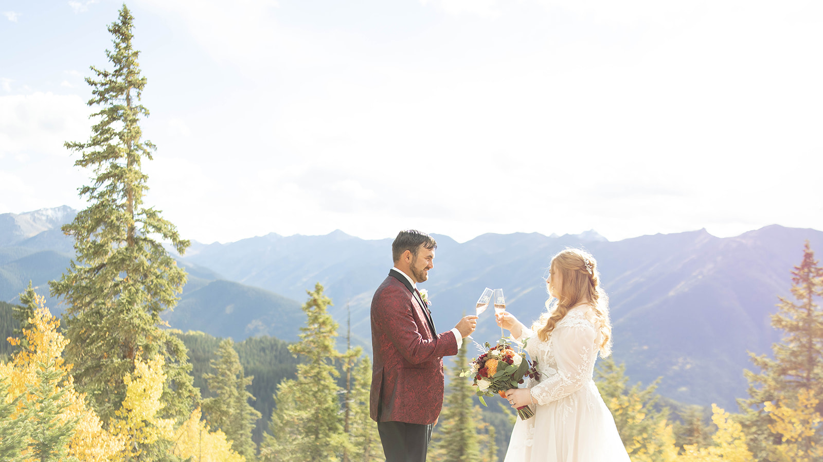 Bride and groom toasting with champagne against a sunlit mountain backdrop during their aspen elopement celebration.