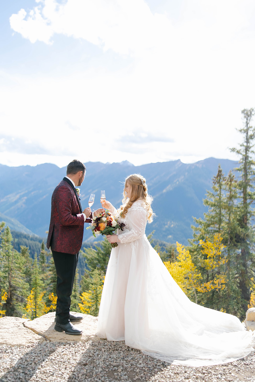 Couple toasting with champagne glasses on a cliffside overlook during their aspen elopement, with sweeping Colorado mountain scenery behind them.