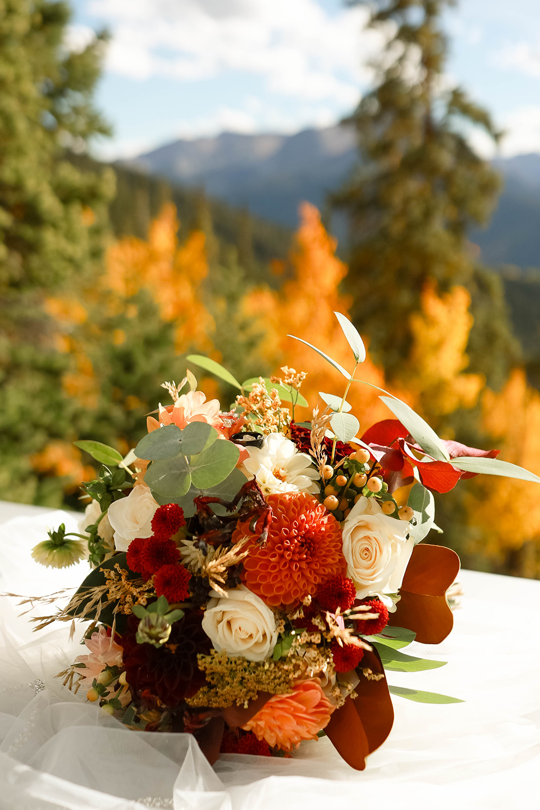 Detailed shot of a fall wedding bouquet set against vibrant yellow aspens and forested mountain slopes.