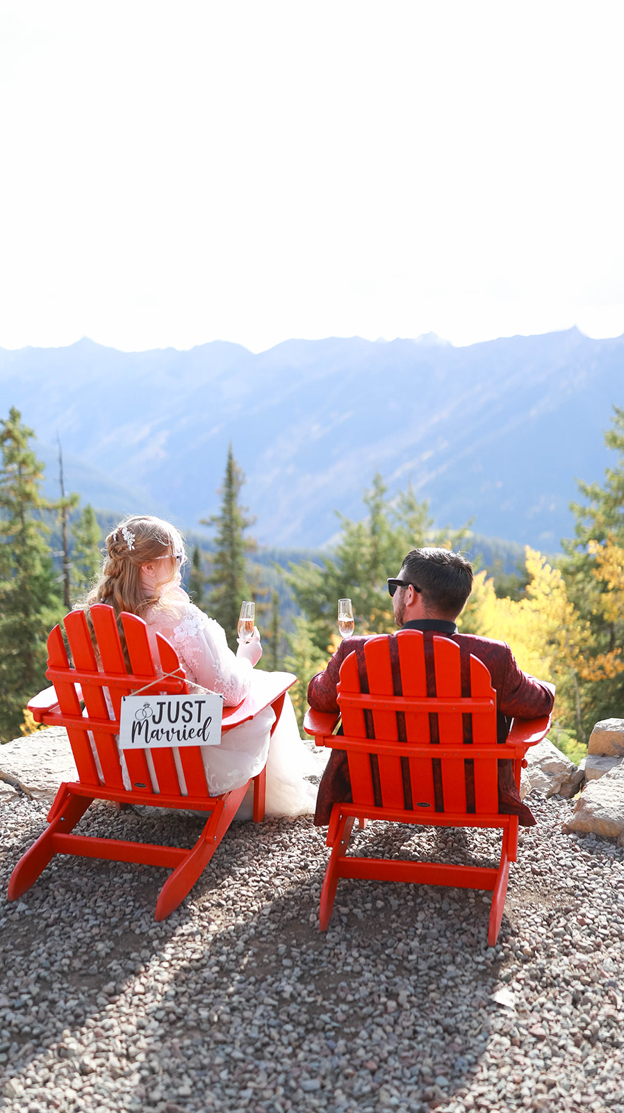 Couple relaxing in red Adirondack chairs, sipping champagne and overlooking sweeping mountain views during their aspen elopement.