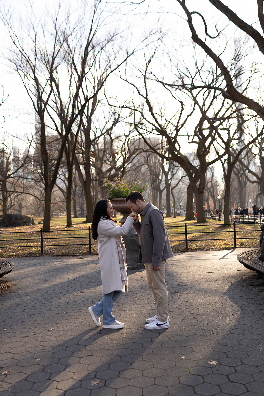Couple laughing together on a tree-lined path, framed by bare branches and soft afternoon light.