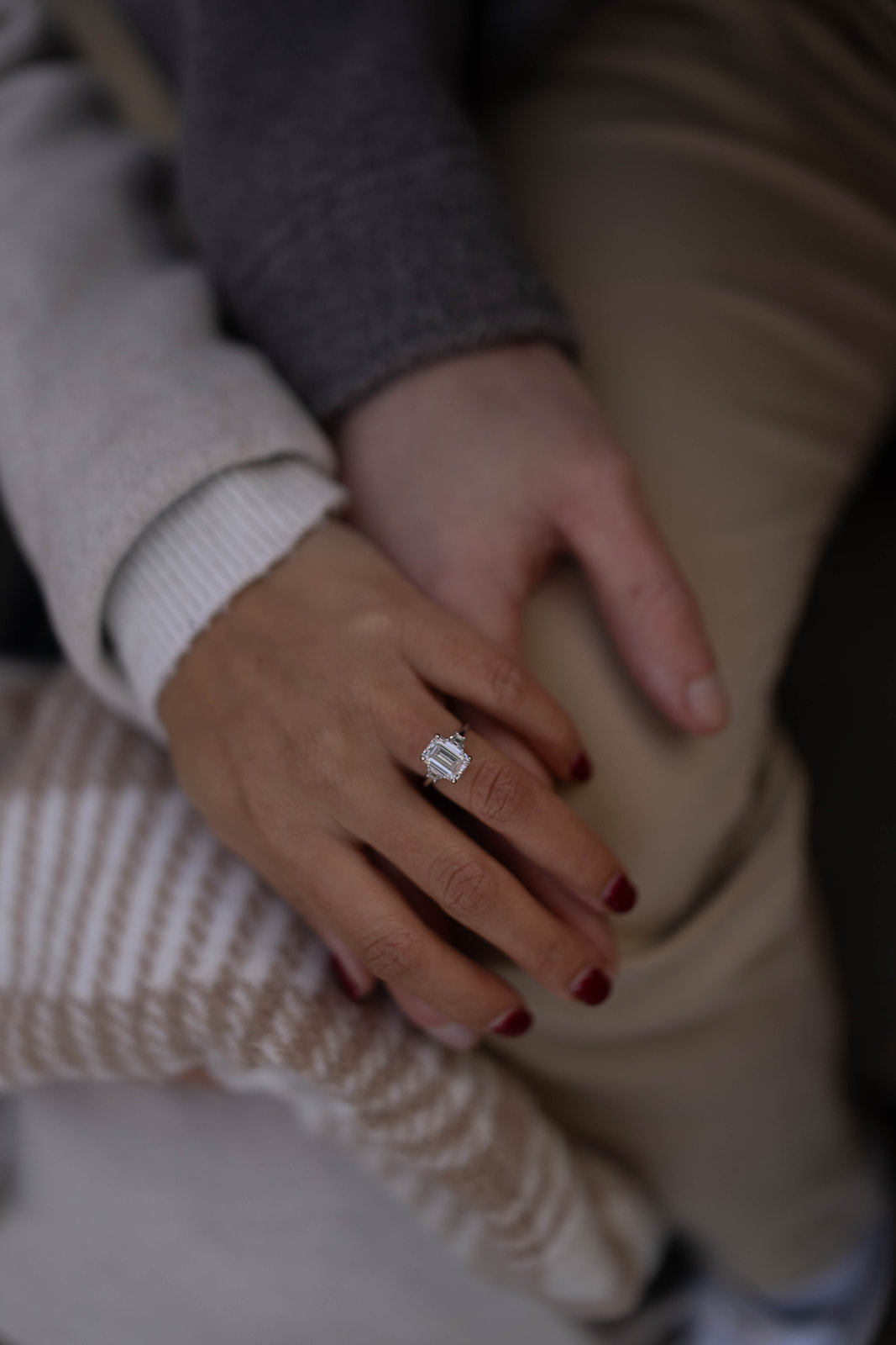 Detail shot of an engagement ring resting on intertwined hands, highlighting the sparkling diamond and cozy winter layers.