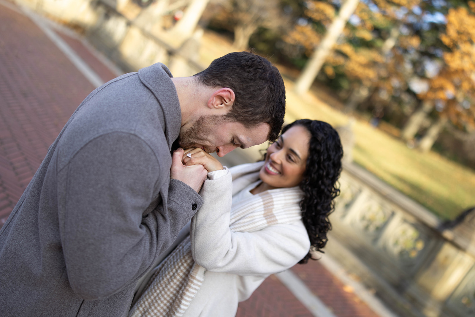 Couple sharing a quiet, romantic moment in an open plaza, framed by winter trees and soft natural light.