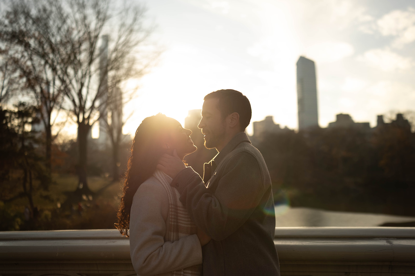 Backlit silhouette of a couple facing each other at golden hour with the city skyline softly glowing behind them.