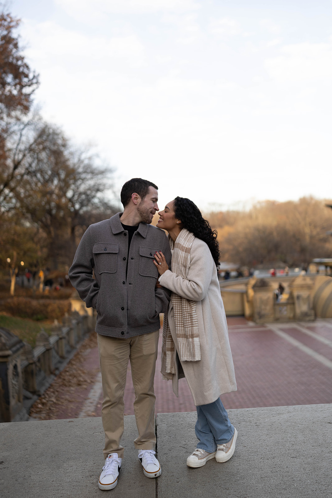 Sweet forehead-to-forehead moment beside the water during a central park engagement, with soft light and winter tones.