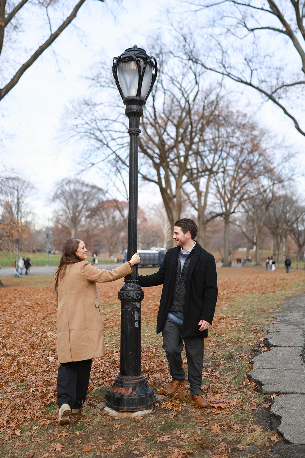 Playful moment as a couple meets at a vintage lamppost during a central park engagement session on a crisp fall afternoon.