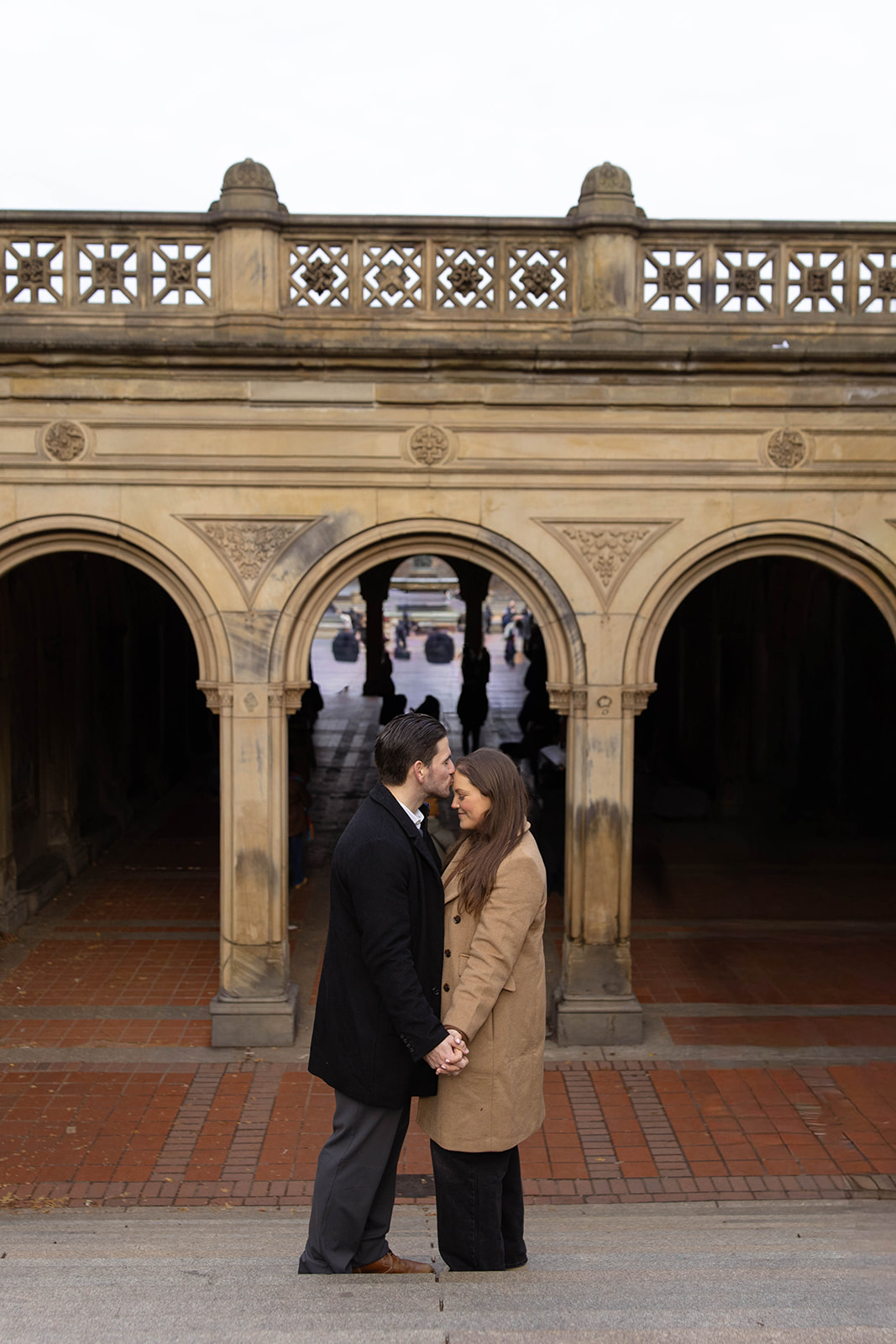 Couple holding hands beneath the historic arches at Bethesda Arcade during their central park engagement, framed by classic architecture and city energy.