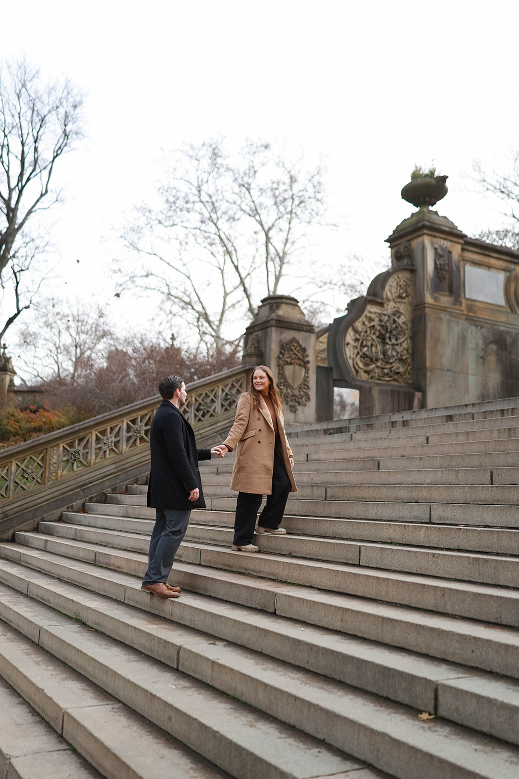 Couple holding hands while walking up the stone steps near Bethesda Terrace during a central park engagement session.