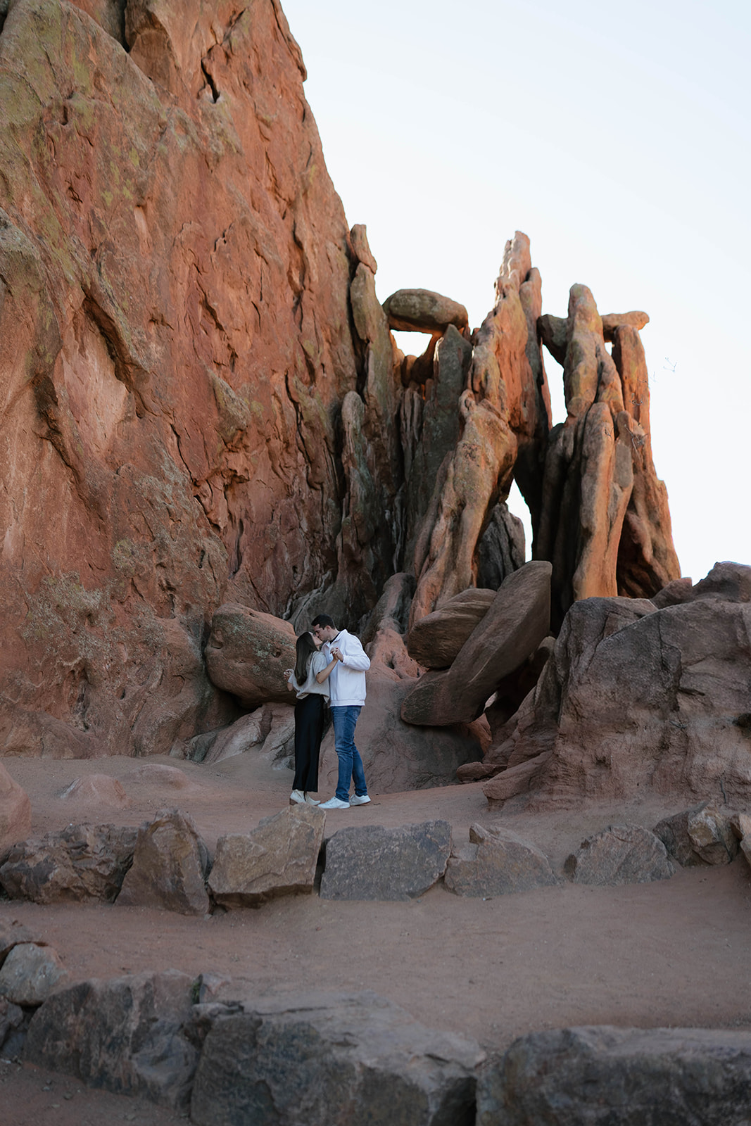 A romantic embrace as a couple stands beneath dramatic vertical rock formations, soaking in the peaceful desert atmosphere.