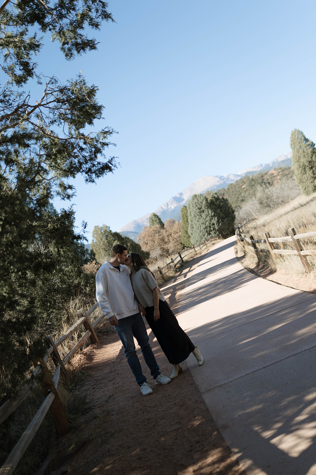 A couple sharing a sweet moment as they lean in for a kiss on a quiet pathway with mountain views stretching behind them at Garden of the Gods.