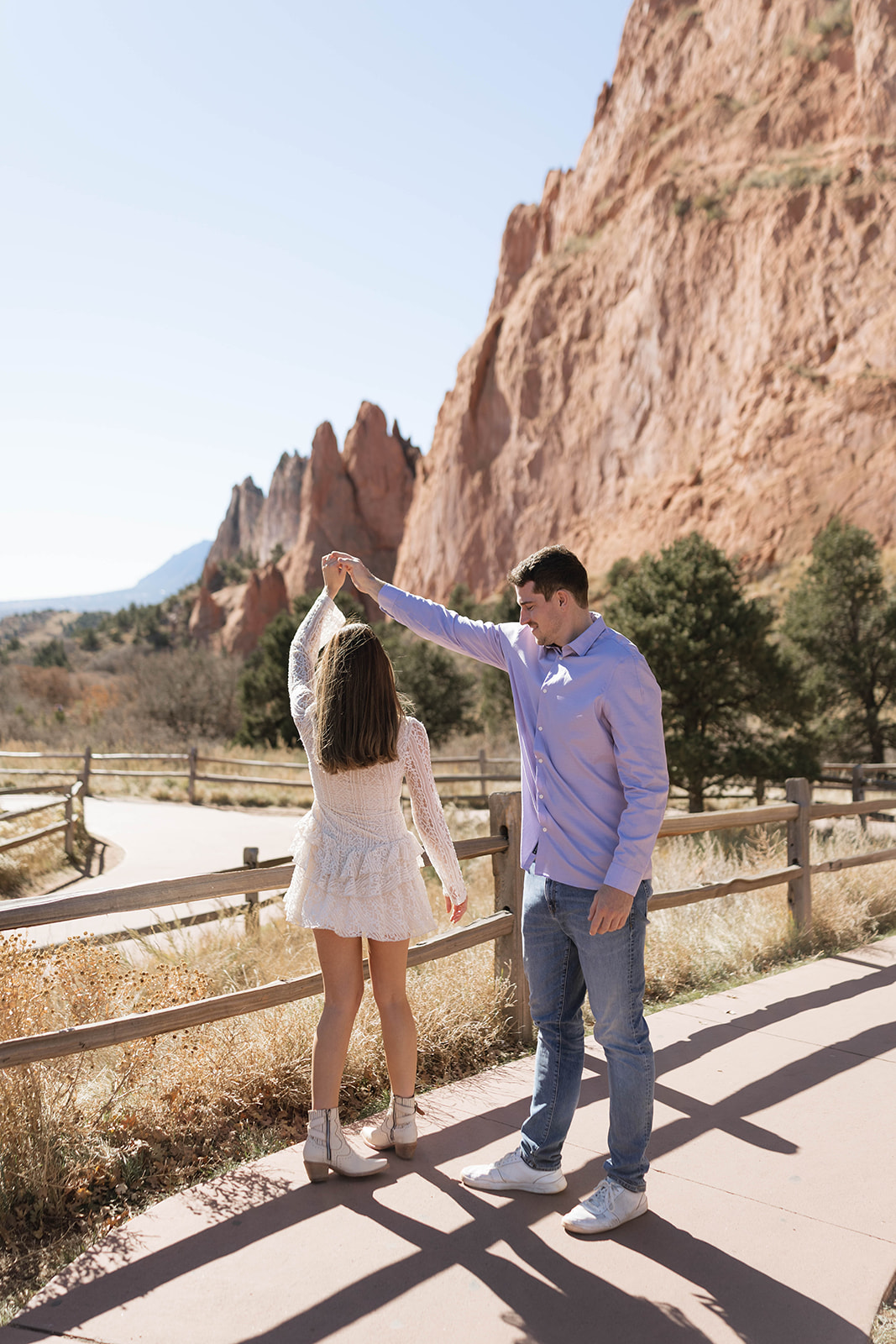 A man twirling his partner as they smile under the sunlight, with scenic rock formations rising in the distance.